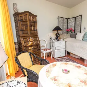 Gemütliches Gästezimmer mit Bett, Holzmöbeln, Tisch und gelben Vorhängen
