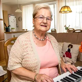 Seniorin spielt Keyboard im Wohnzimmer, häusliche Pflege und Betreuung zuhause