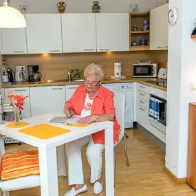 Seniorin sitzt am Esstisch in heller Küche und macht Kreuzworträtsel
