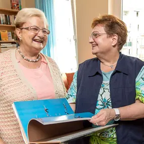Zwei Seniorinnen blättern in einem Bildband in einer Bibliothek im Pflegeheim