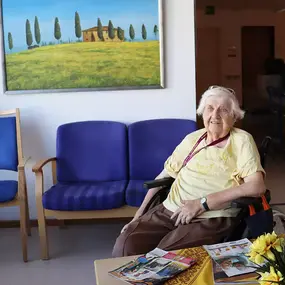 Seniorin im Rollstuhl im Wartebereich eines Pflegeheims mit Zeitschriften