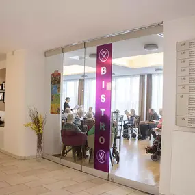 Bistro im Pflegeheim: Senioren sitzen am Tisch hinter Glas-Schiebetür