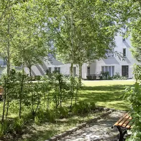 Grüner Innenhof mit Bäumen, Sitzbänken und Wohnhaus im Hintergrund